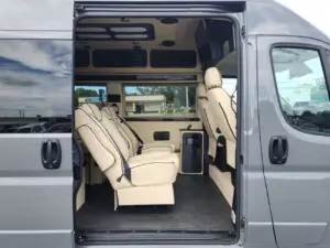 Interior view of a luxury tour bus featuring beige leather captain chairs and modern amenities.
