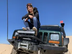 Woman with goggles sitting on Jeep at Silver Lake Sand Dunes during off-roading in Southwest Michigan