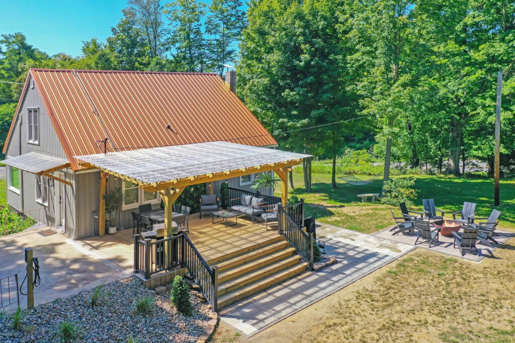 Copper Top Ridge patio under a clear-roof pergola with lounge seating and a nearby fire pit in wooded New Buffalo, Michigan. Image title: Copper Top Ridge Patio & Pergola – New Buffalo, MI Caption: Spacious pergola-covered deck and fire-pit lounge at Copper Top Ridge—your modern cottage retreat in New Buffalo, MI.